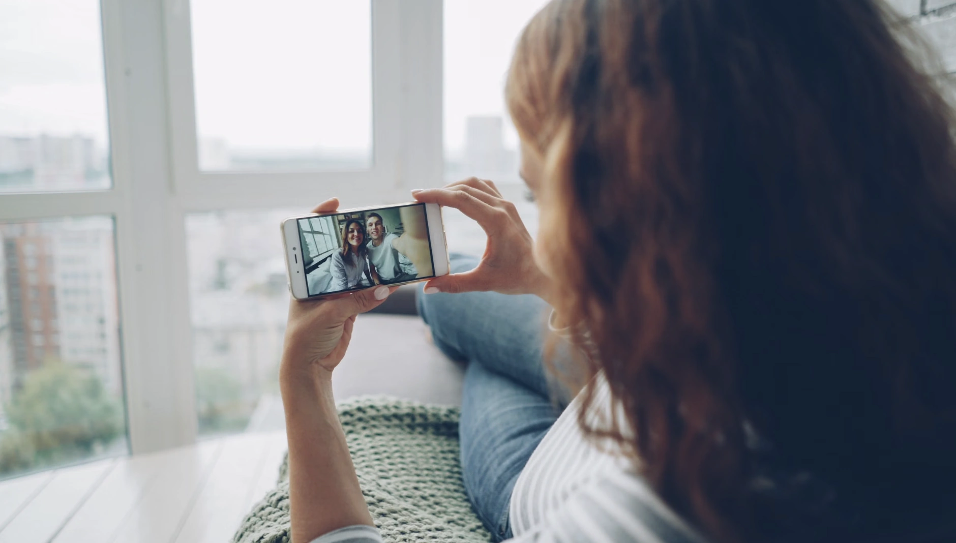 Woman lying by a window taking a selfie with her phone